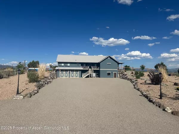 Blue-gray home at the end of a wide driveway, surrounded by dry rock landscaping.
