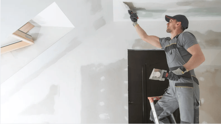 Interior under renovation with a worker smoothing drywall near a skylight.