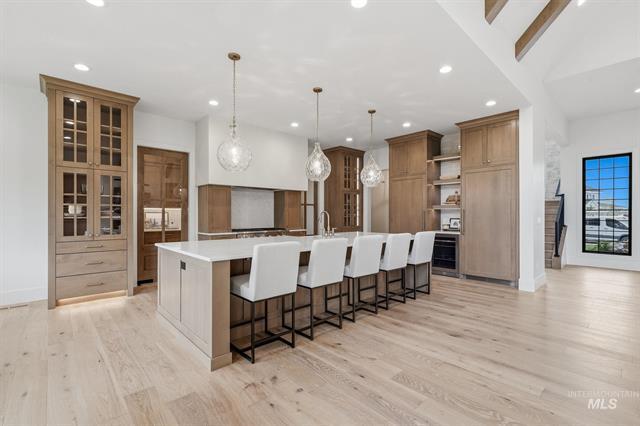 Luxury kitchen with a long white island, six seats, warm wood cabinetry, and pendant lights.