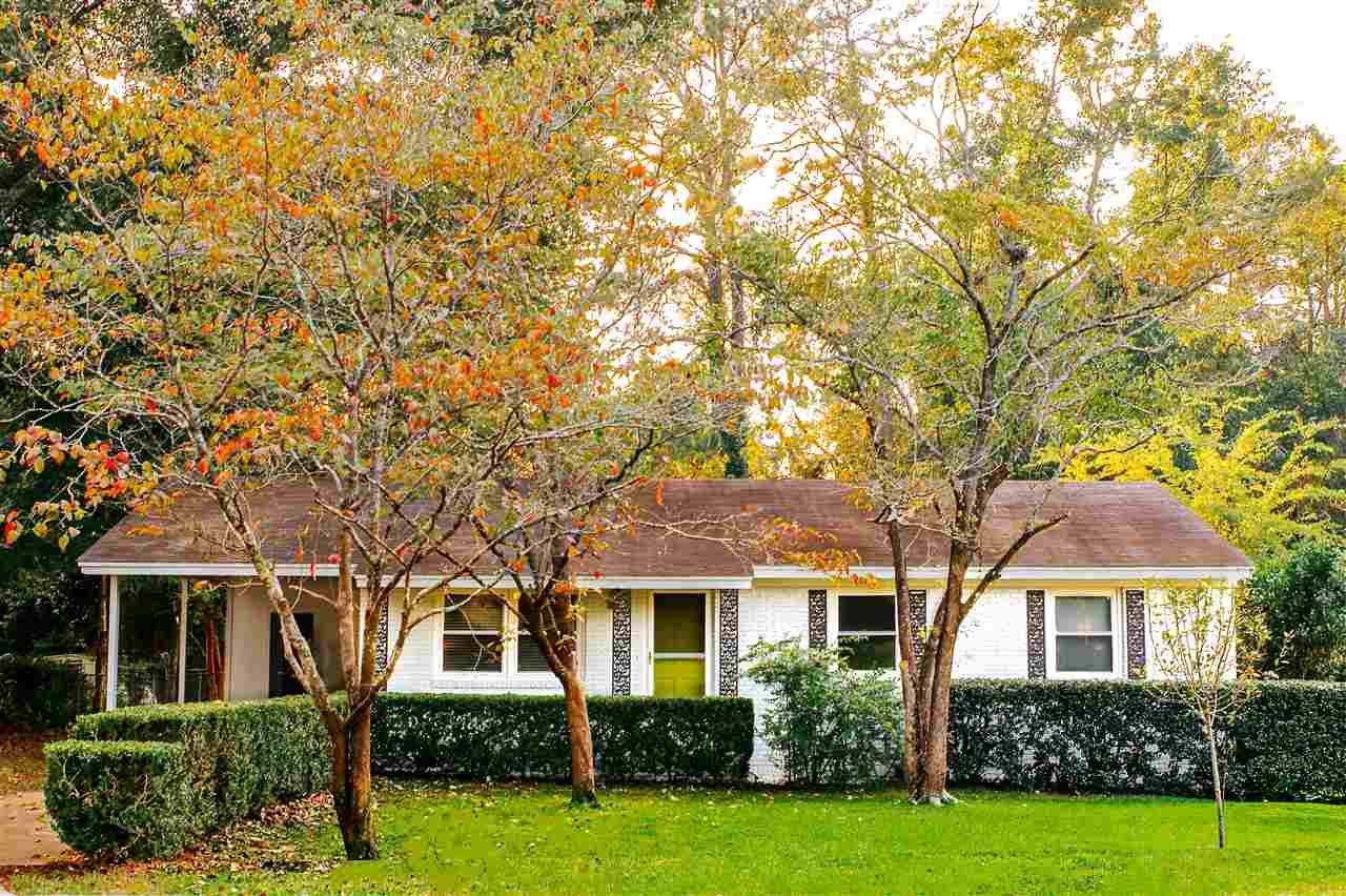 A small white house surrounded by a green lawn and trees, creating a serene and inviting outdoor environment.