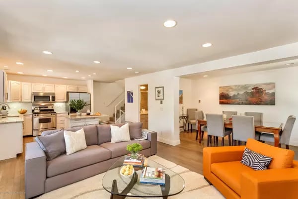 Open-plan living area with a gray sofa, orange armchair, and kitchen with light wood cabinets.