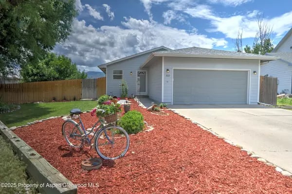 Gray single-story home with a two-car garage, red-mulch garden, and bicycle by the driveway.