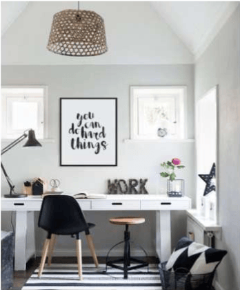 Bright home office with a long white desk, black chair, woven pendant light, and framed motivational print.