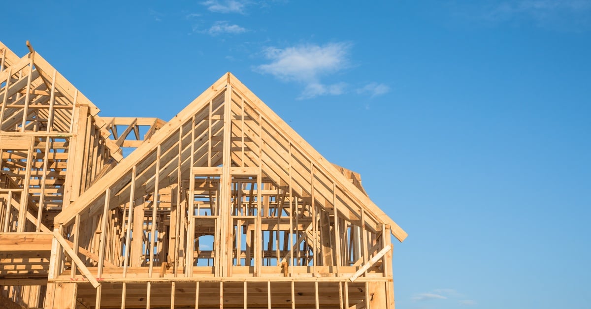 A close-up of the roof and second level of an unfinished home with wooden trusses, posts, and beam framework.