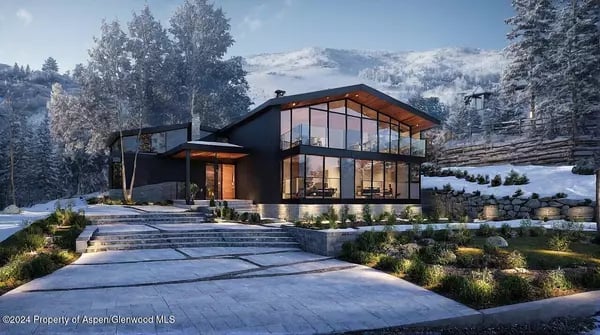 Modern glass-fronted mountain home with a stone driveway and snow-covered mountains beyond.