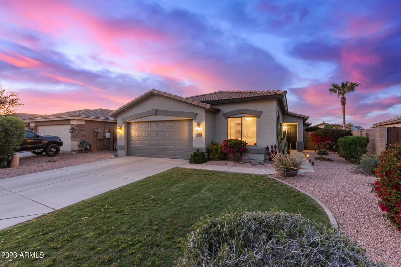 Single-story stucco home with a two-car garage and desert landscaping beneath a vivid sunset sky.