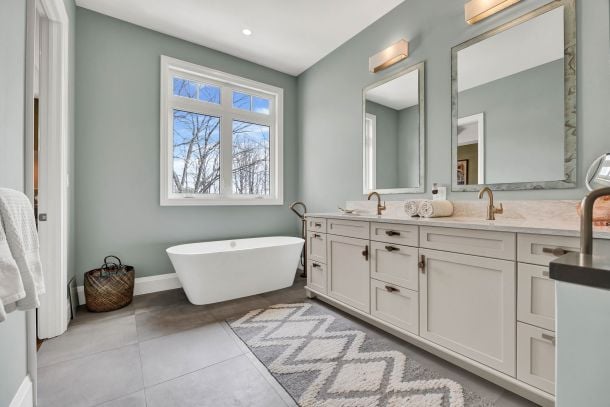 Bathroom with a freestanding tub beneath a window and a long double vanity with brass fixtures.