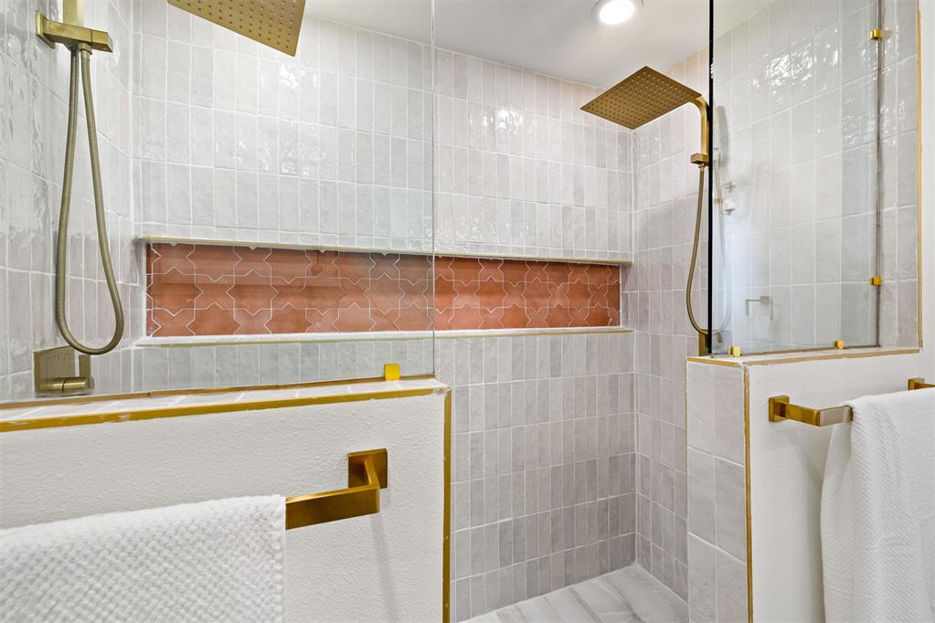 Tiled bathroom shower with brass fixtures, dual showerheads, and a terracotta accent niche.