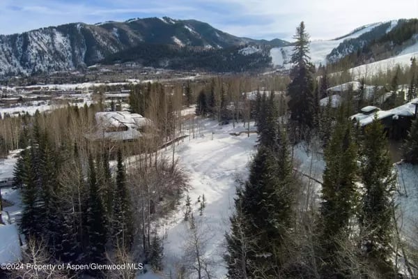 Snow-covered mountain valley with scattered homes and evergreen trees, viewed from above.