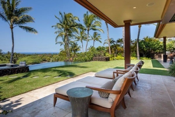 Covered patio with cushioned loungers overlooking a palm-lined lawn and ocean.