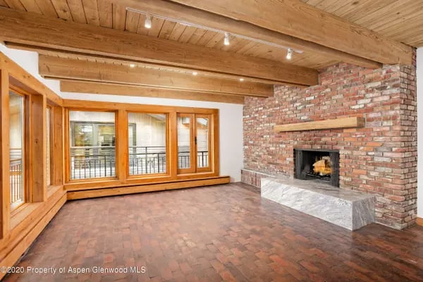 Living room with a wood ceiling, brick fireplace, and large wood-framed windows.