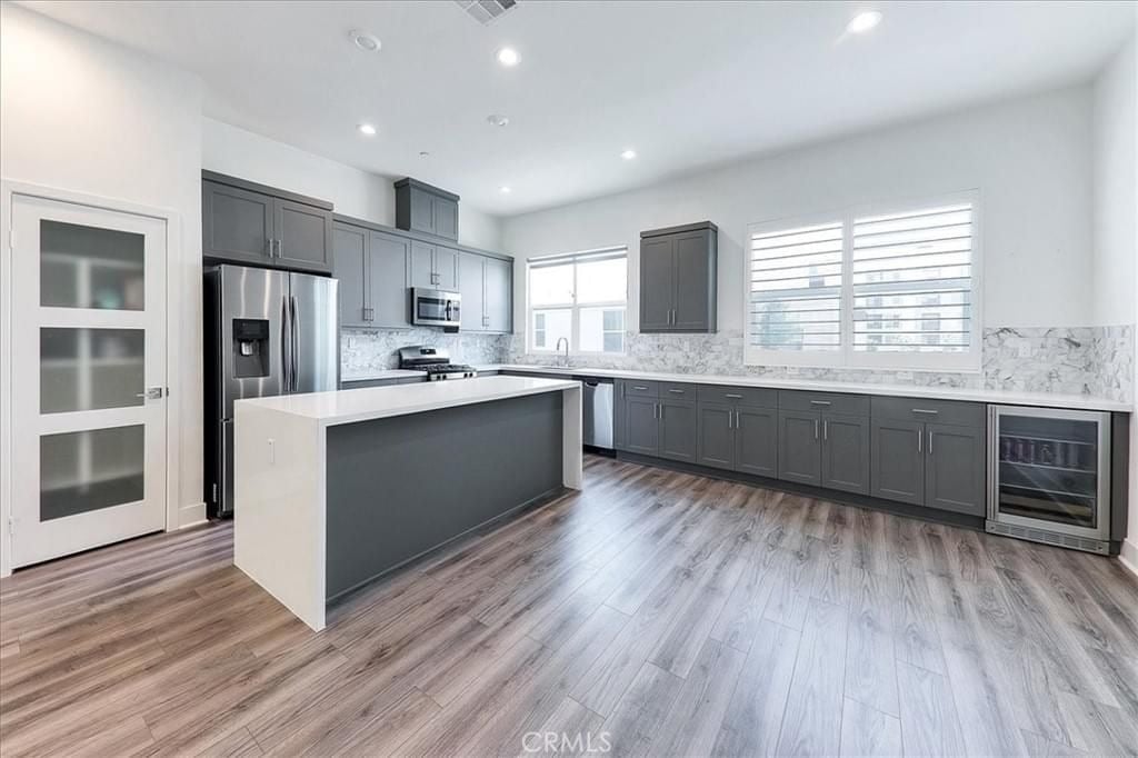  A spacious modern kitchen with dark gray cabinets, a large white island, and a wine fridge built into the counter.