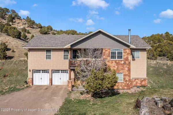 Two-story tan home with stone accents and two garage doors on a grassy hillside.