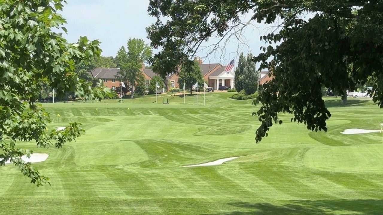 Golf course with striped fairways, sand bunkers, mature trees, and brick clubhouse buildings.