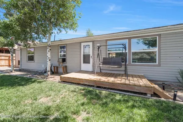 Rear exterior of a single-story home with a raised wooden deck and black porch swing.