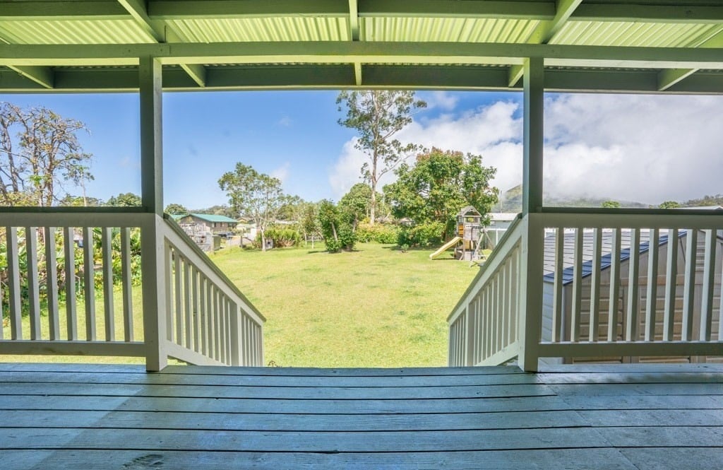 Covered deck overlooking a large grassy backyard with a children's play structure and solar panels nearby.