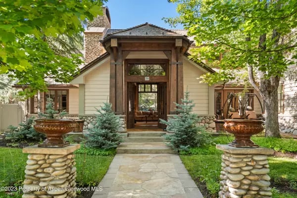House with a timber-framed entrance, stone chimney, and garden fountains beside the walkway.