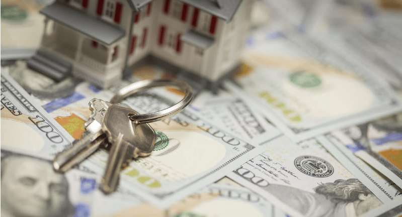 House keys on $100 bills, with small model houses in the background.