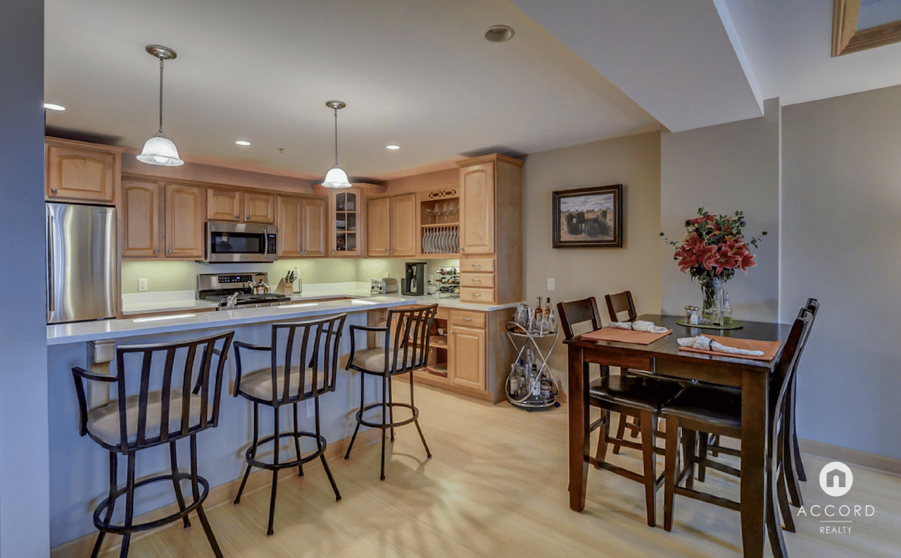 Condo kitchen and dining area with a breakfast bar, wood cabinetry, and stainless steel appliances.