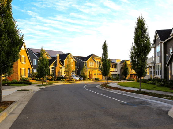Residential street curving past yellow and gray homes with evergreen trees.