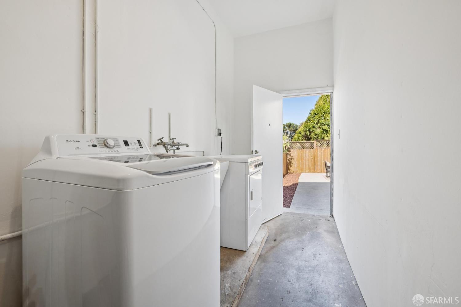Laundry room with a top-loading washer and dryer beside an open door to a fenced outdoor area.