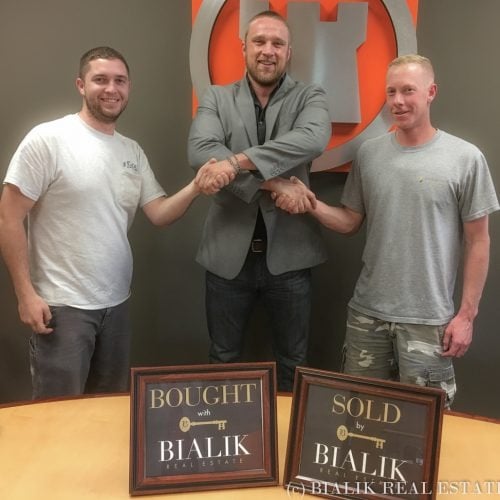 Three men celebrate a home closing behind Bialik Real Estate bought and sold signs.