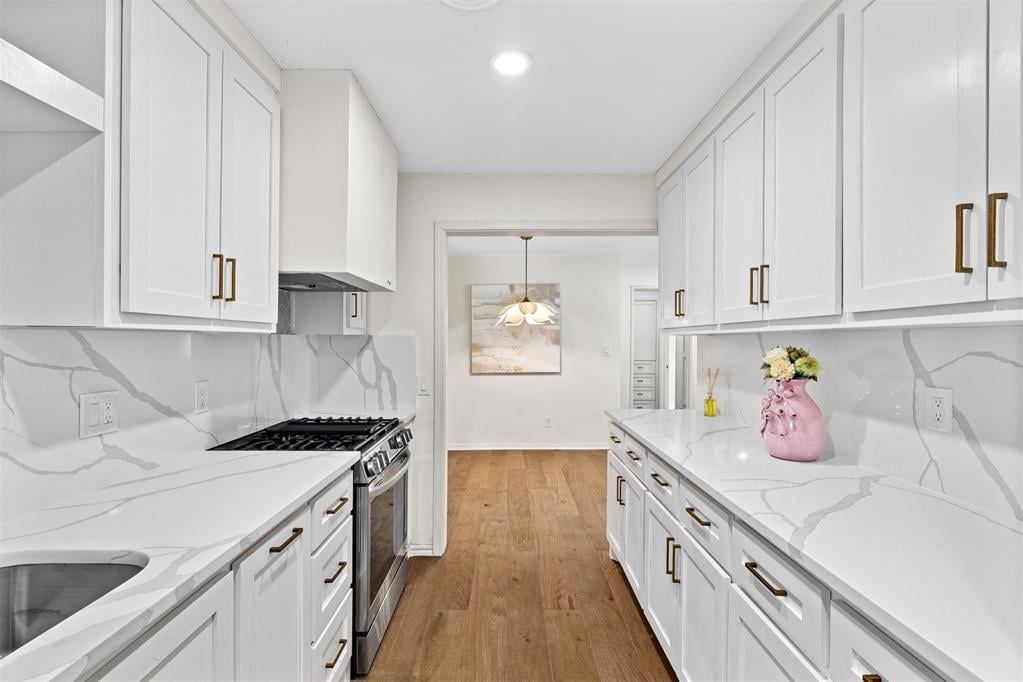 Galley kitchen with white shaker cabinets, veined countertops, brass hardware, and warm wood floors.