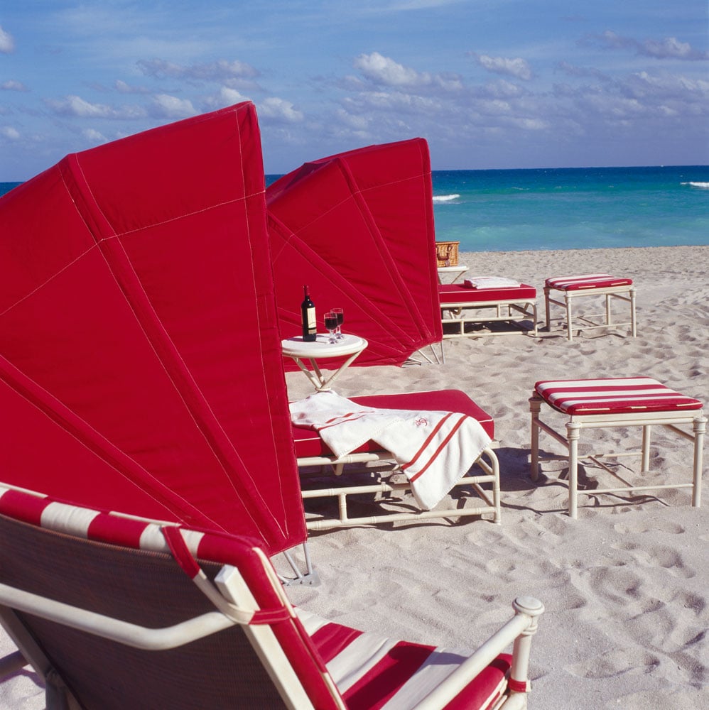 Red-and-white beach loungers on the sand beside turquoise ocean water.