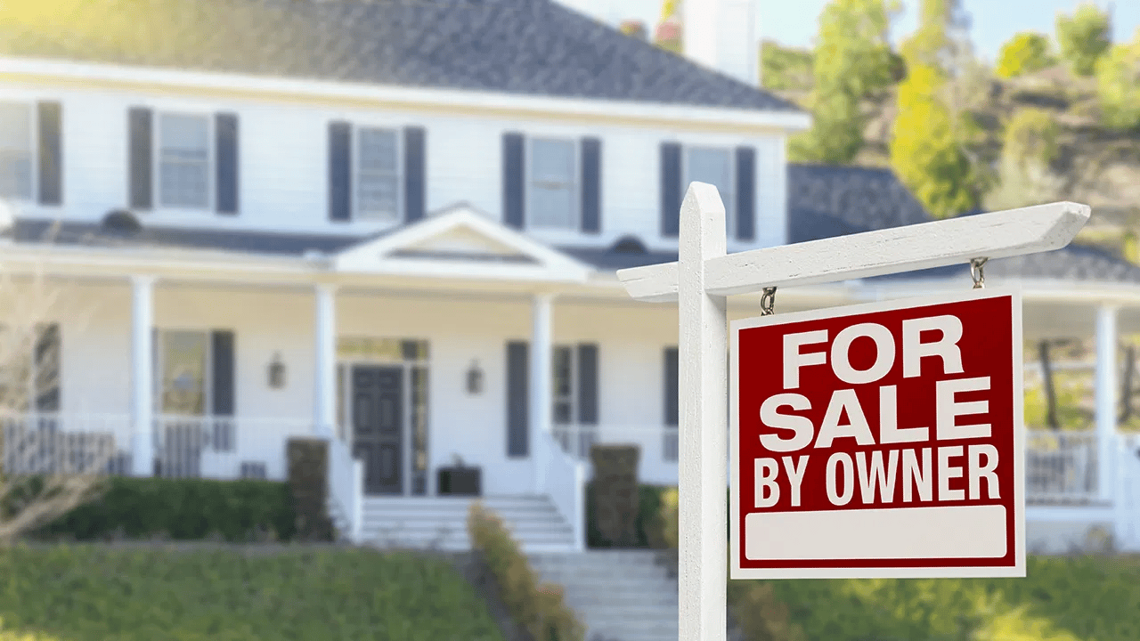 White two-story house behind a prominent For Sale By Owner sign.