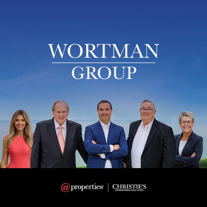 Five Wortman Group agents posed beneath their logo against a blue sky and waterfront.