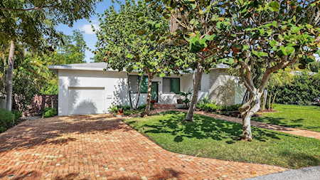 Single-story home with a wide brick-paver driveway, mature trees, and a front lawn.