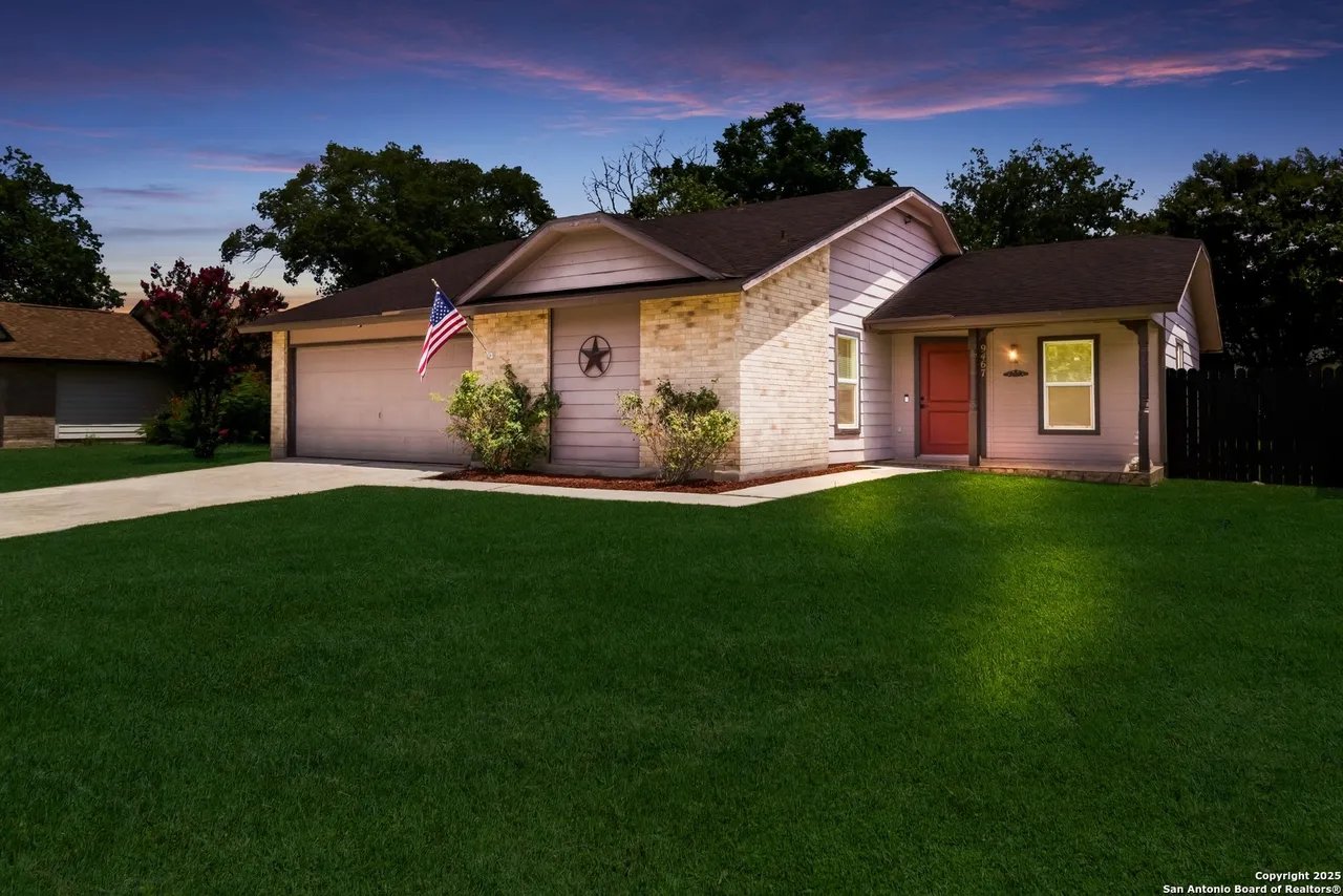 Single-story brick-and-siding house with an attached garage, red front door, and broad lawn at dusk.