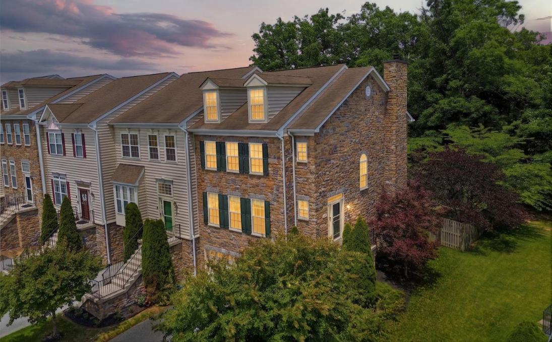 Attached townhomes at dusk, with a stone facade, dark shutters, and warmly lit windows.