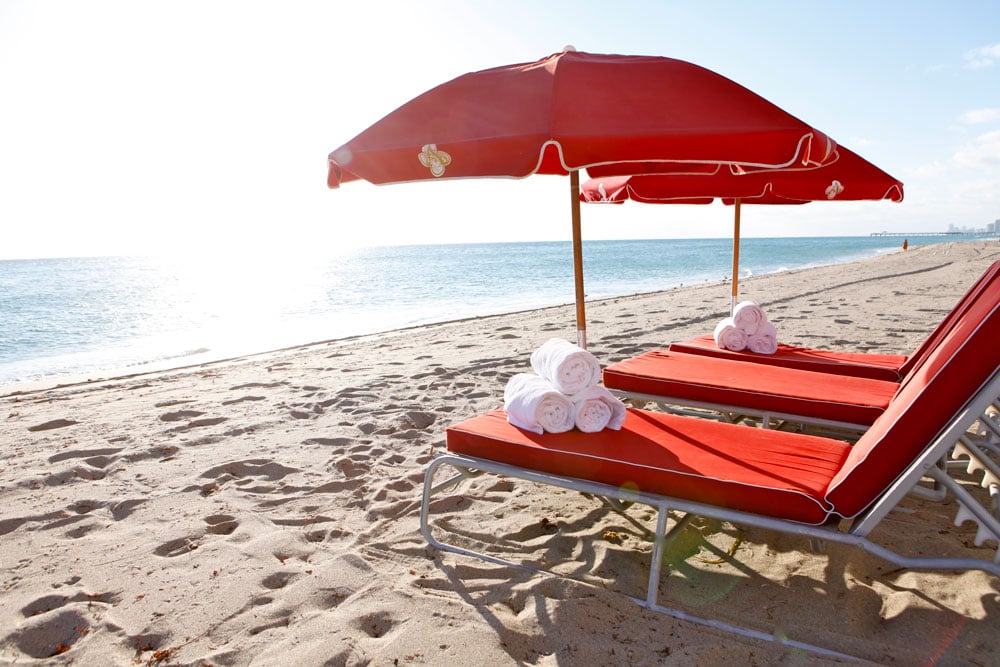Red loungers and umbrellas with white towels on a sandy beach beside the ocean.