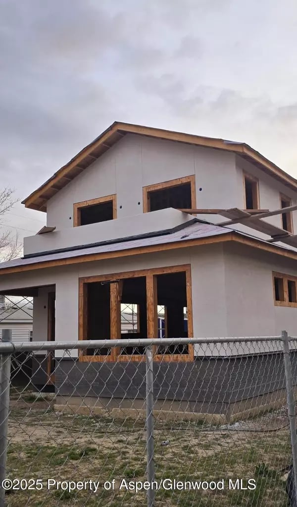 Two-story home under construction behind a chain-link fence.