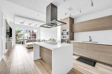 Modern kitchen with a large white island, wood cabinetry, and an open view into the living area.