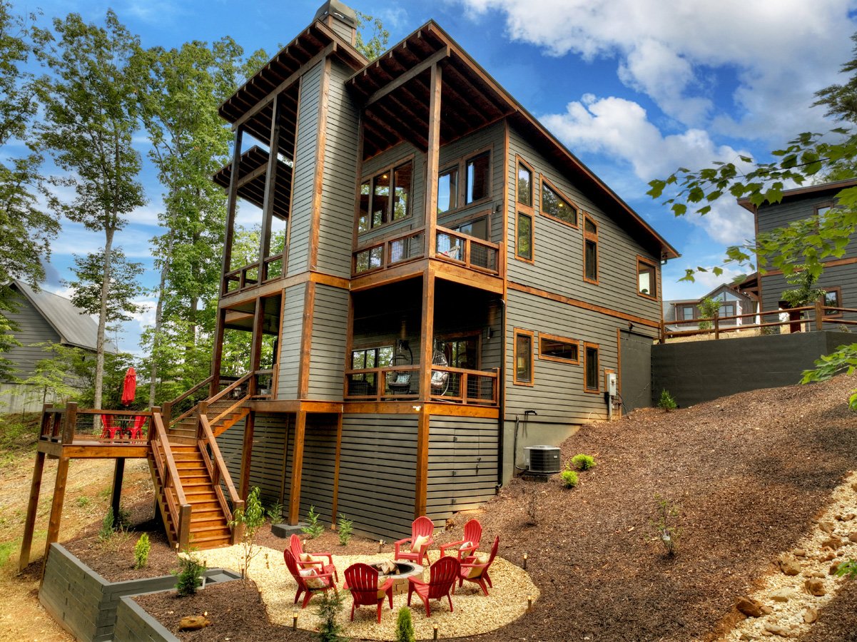 Mountain home with elevated decks, timber trim, and a gravel seating area with red Adirondack chairs.