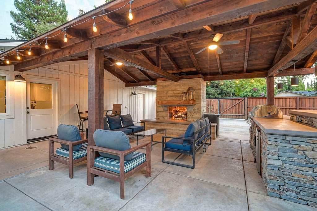 Covered patio with blue-cushioned seating, a stone fireplace, and a built-in grill.