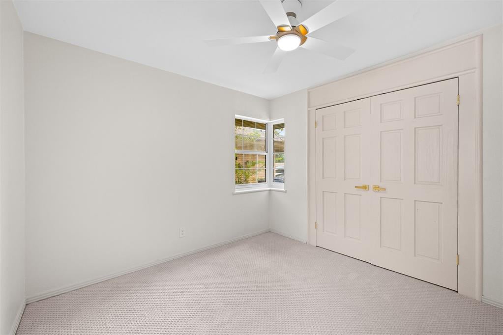 Empty bedroom with carpet, double closet doors, a corner window, and a ceiling fan.