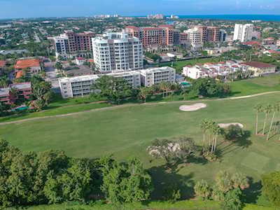 Aerial view of East Boca buildings beside a golf course, ocean visible on the horizon.