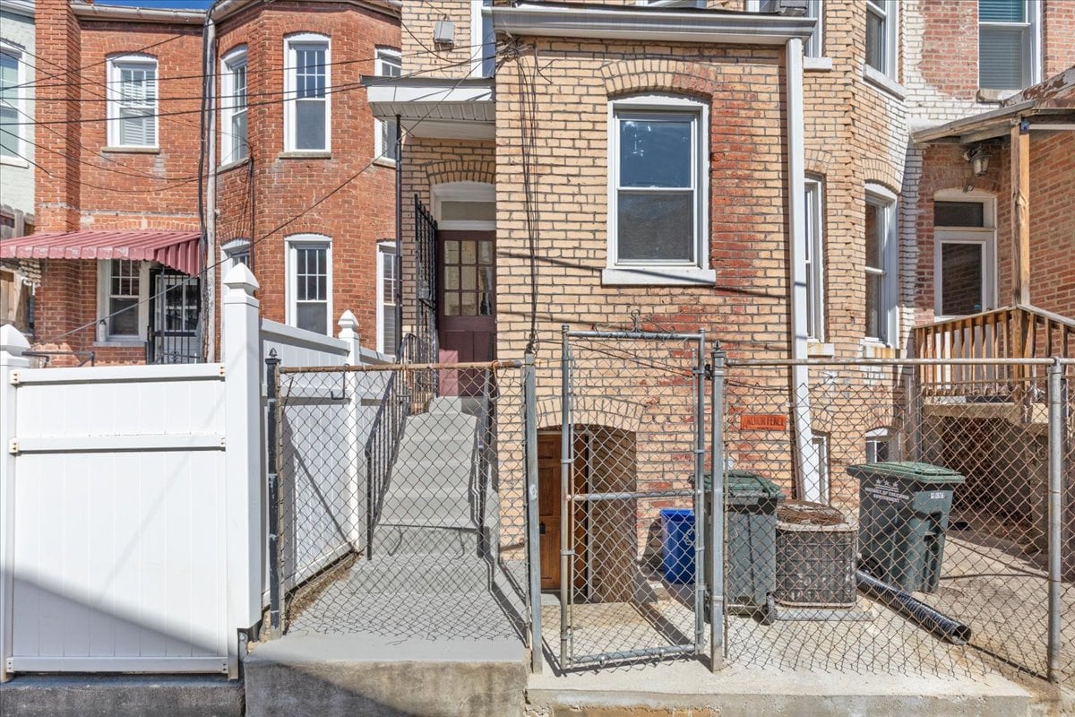 Brick rowhouse entrance with a gated concrete walkway, white privacy fence, and neighboring homes.