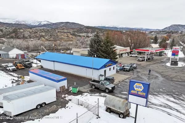 Collbran commercial buildings, including a NAPA Auto Parts store and Exxon station, with snowy mountains beyond.