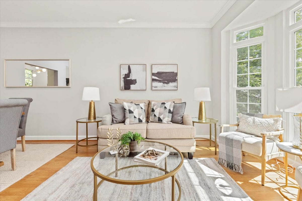 Staged living room with a beige sofa, glass coffee table, and large windows.