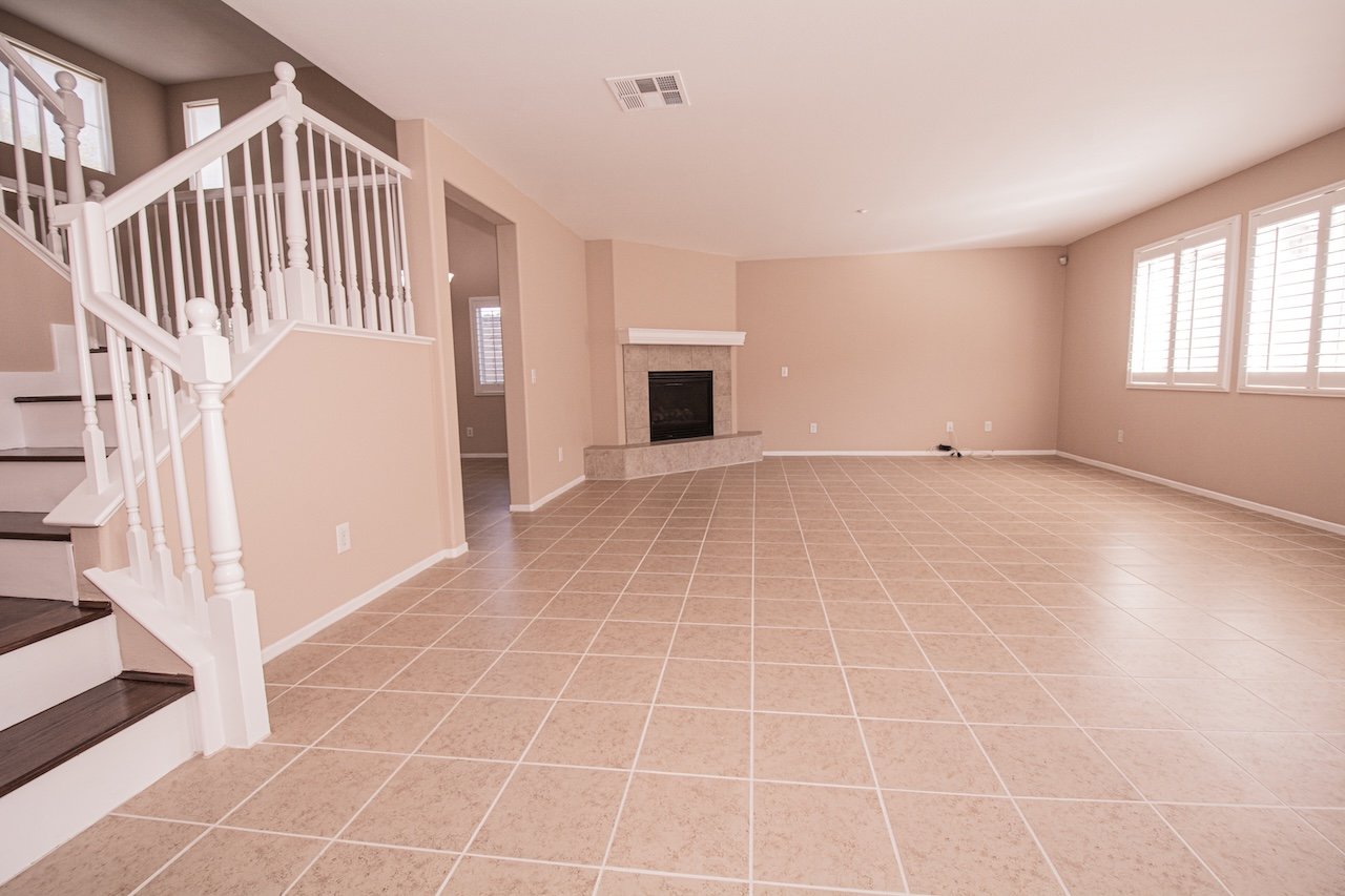 Vacant living room with tiled floors, a white staircase, corner fireplace, and shuttered windows.