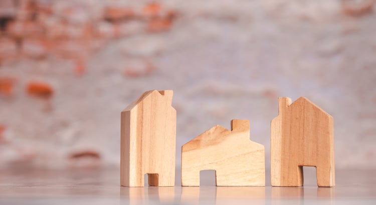 Wooden houses arranged on a table against a backdrop of a rustic brick wall.