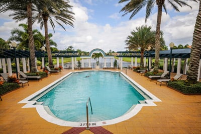 Community pool framed by palm trees, lounge chairs, and covered seating areas.