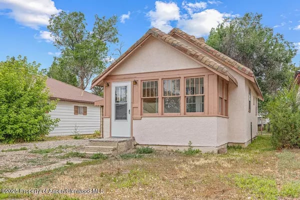 Small pale pink stucco home with a tile roof and a row of front windows.