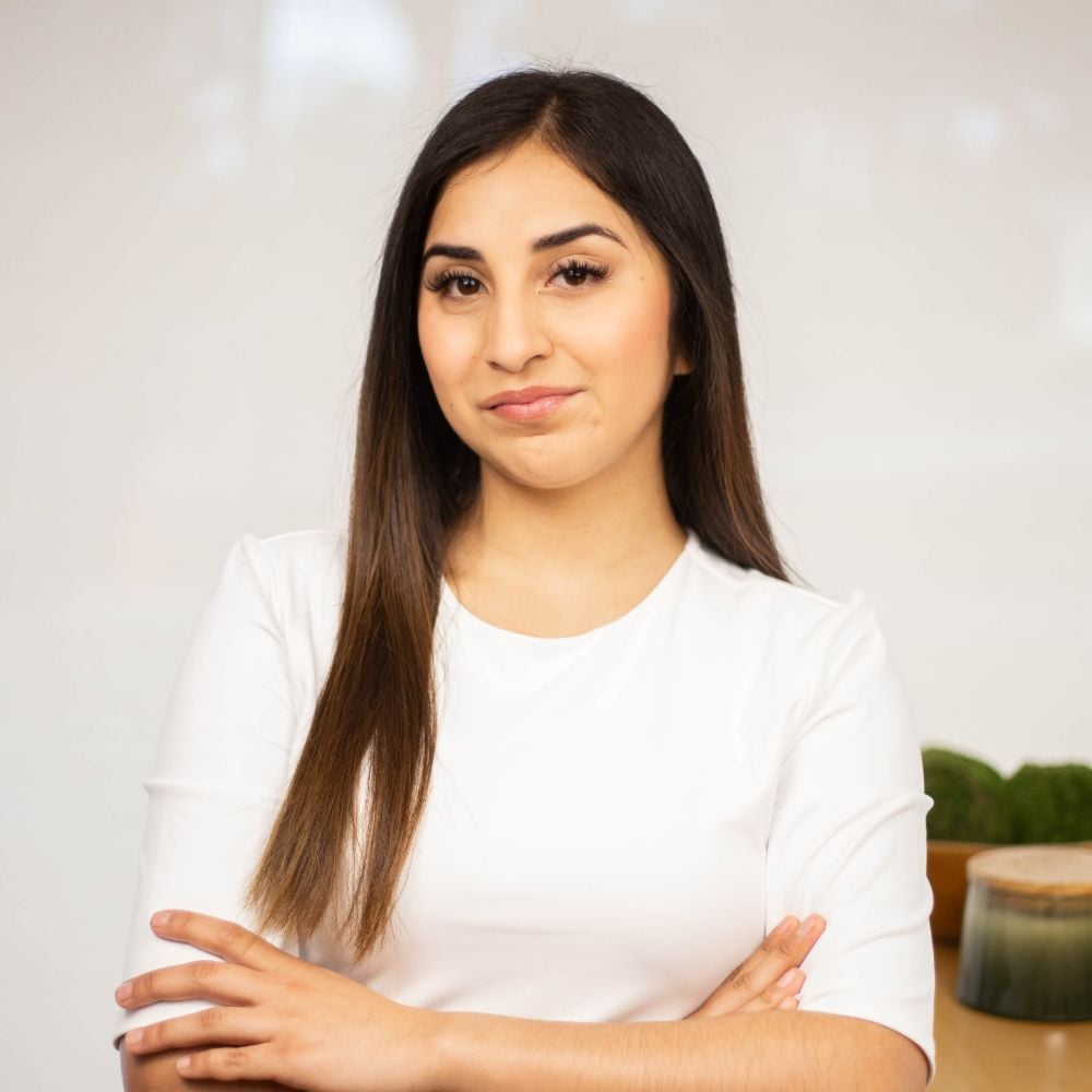 Vicky Gomar with long dark hair, wearing a white top with her arms crossed.