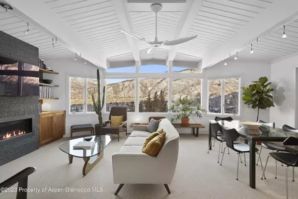 Open-plan living room with vaulted ceiling, stone fireplace, and mountain views through large windows.