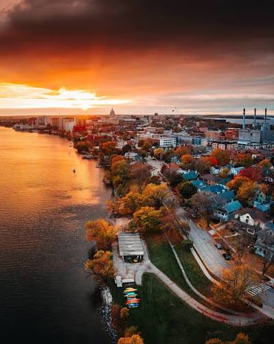 Aerial view of a lakeside city at sunset, with autumn trees and waterfront homes.